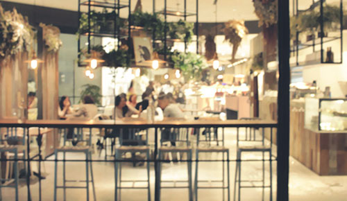 A modern, well-lit café with several people sitting at tables, surrounded by hanging plants and contemporary décor, features stylish pieces from Trinidad Event Furniture. - Perched Event Rentals, Trinidad