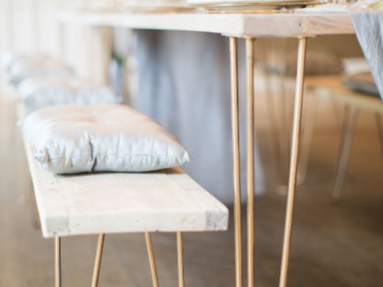 Close-up of the Hairpin Bench with a wooden seat and a light cushion, beside a matching table with slim gold metal legs
