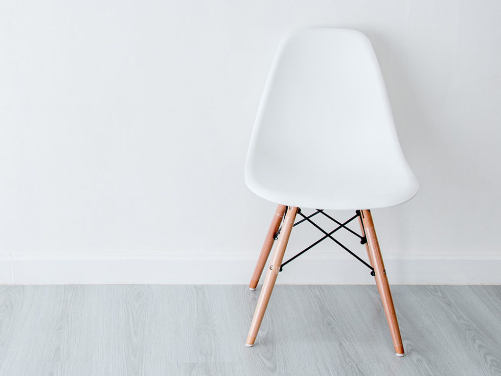 Eames Chair with a white plastic seat and wooden legs on a light grey wood floor against a plain white wall
