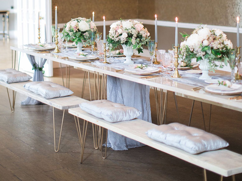 Hairpin Table set for a formal event with floral centrepieces, candles and cutlery, with cushioned benches on both sides