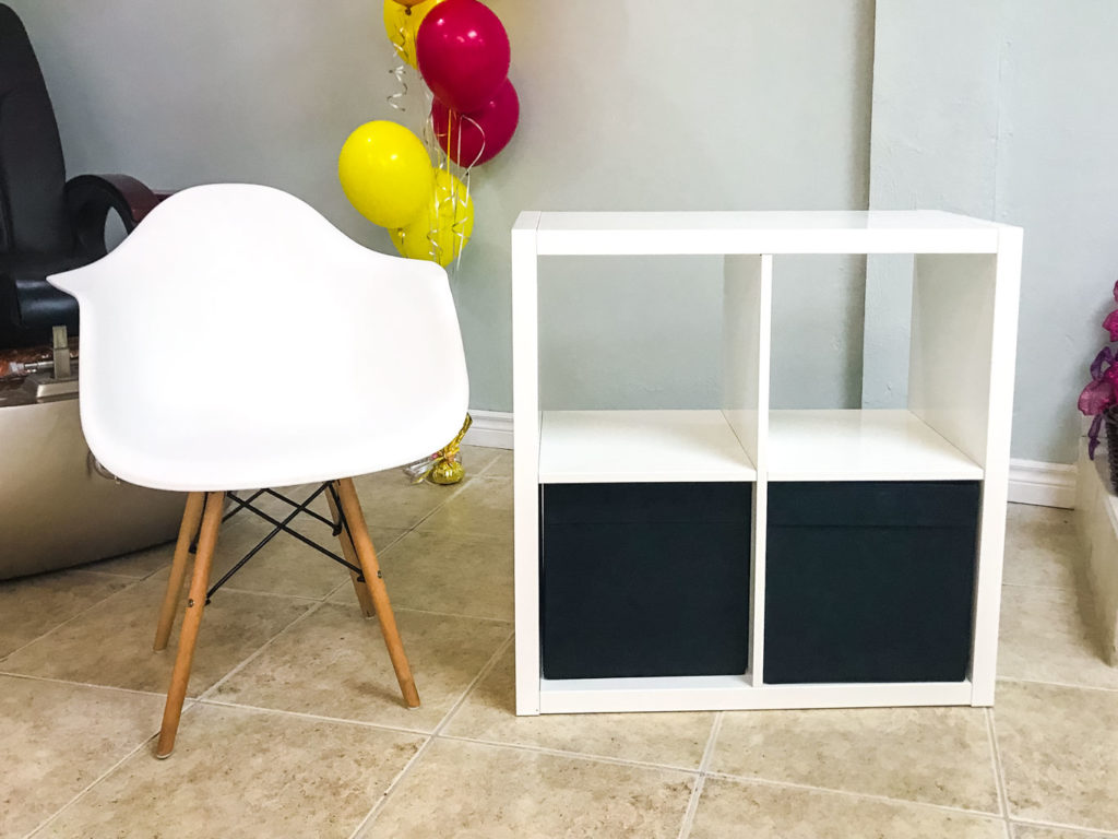 Simple Storage Table with two black bins beside a white chair with wooden legs, with red and yellow balloons behind