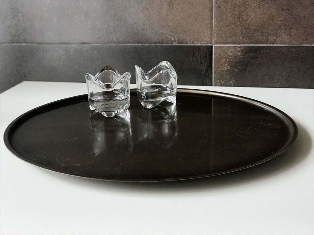The Candle Tray with two small, clear glass candle holders on a round black tray