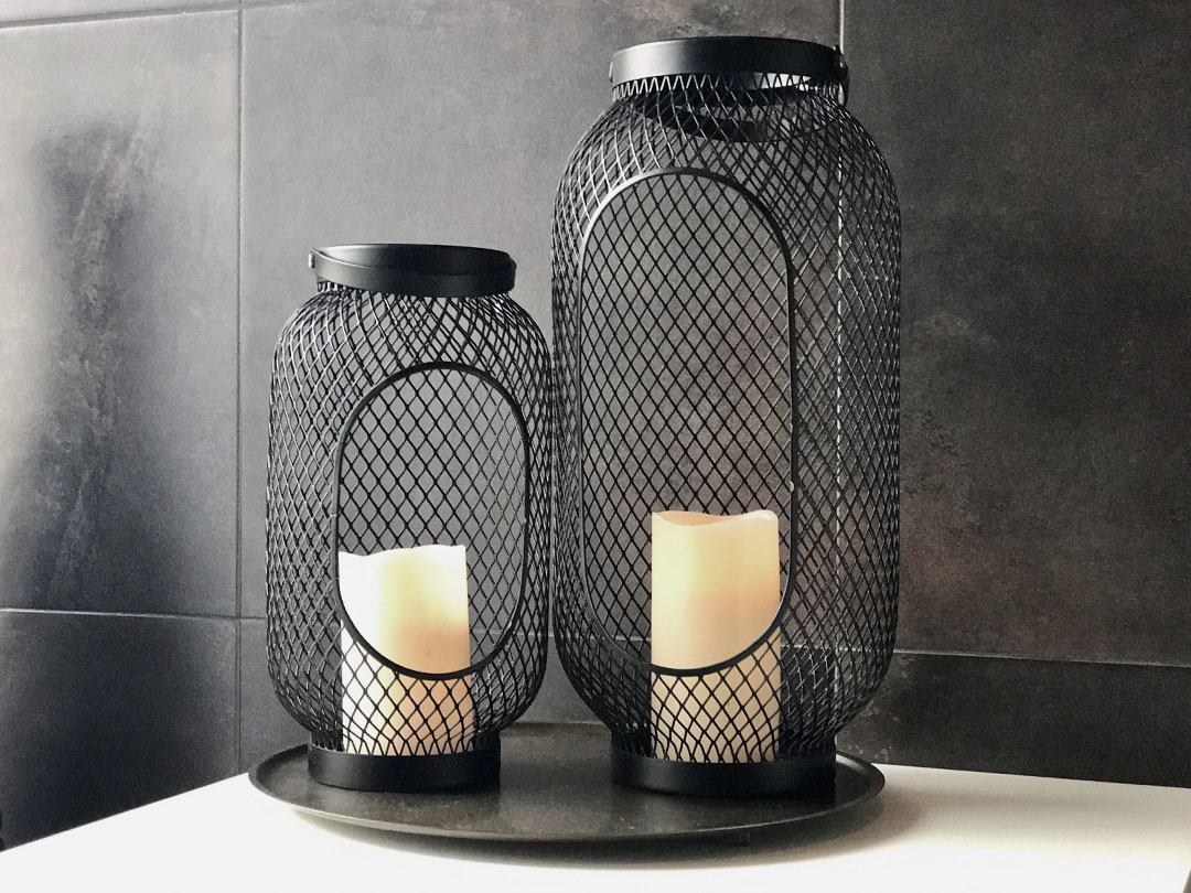 A pair of candle lanterns with white LED candles, arranged on a round black tray against dark tiles—an elegant accent ideal for Trinidad Event Hire. - Perched Event Rentals, Trinidad