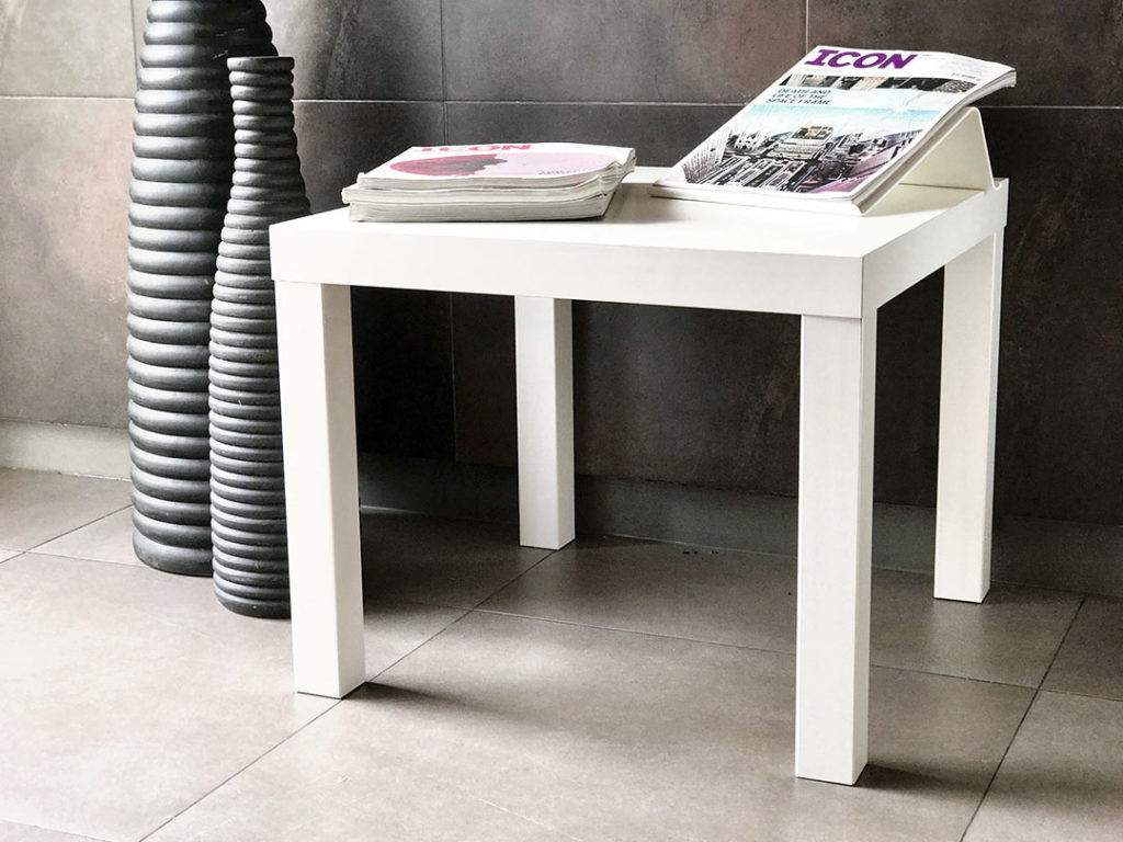 Simple Side Table, white and rectangular, holding stacked magazines on a tiled floor beside a tall, textured black vase