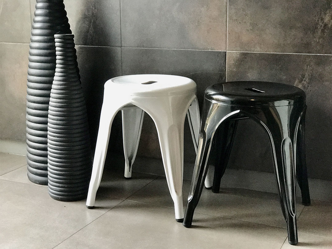 Two Industrial Stools, one white and one black, side by side next to three tall, ribbed vases against a tiled wall