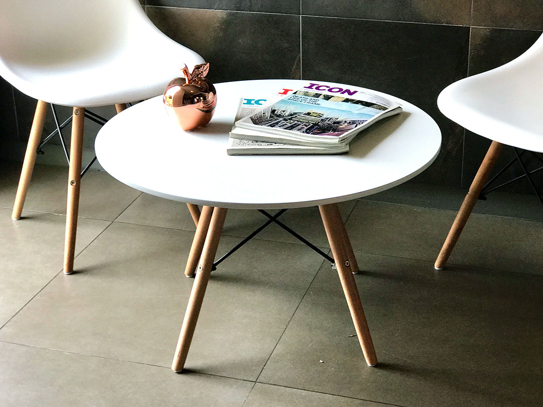 Eames Coffee Table, a white round table with wooden legs, holding a magazine and a small apple, beside two white chairs