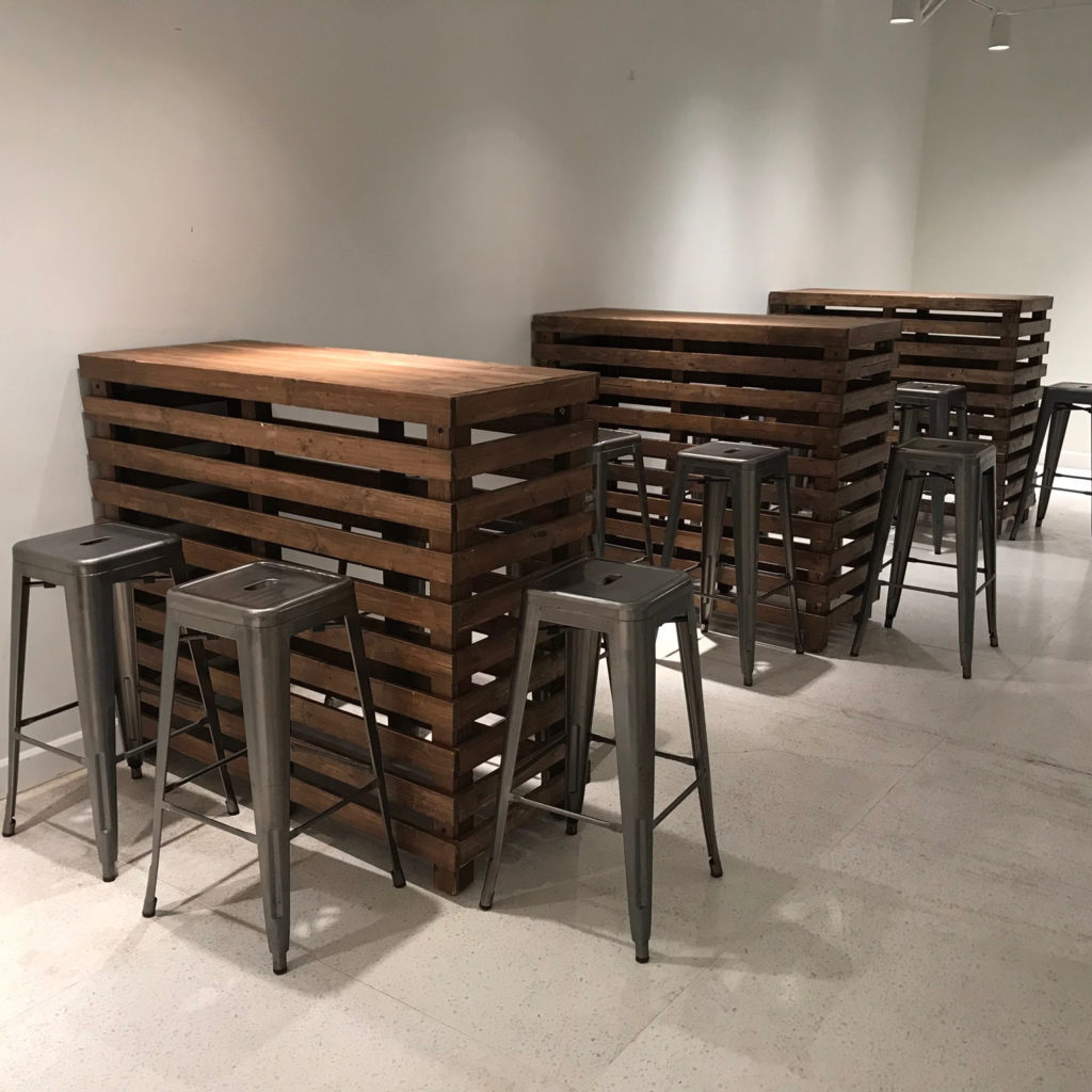 Four Pallet Bar Tables, each paired with metal stools, arranged in a room with light-coloured walls and flooring