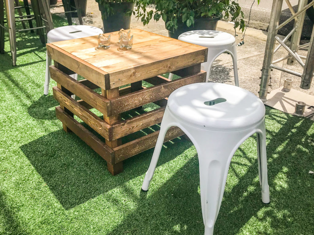 A Pallet Box with two glass tumblers, surrounded by white metal stools on artificial green grass in an outdoor set-up