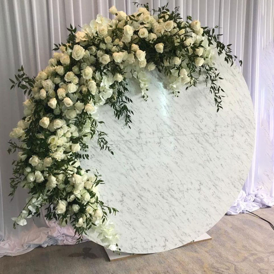 The Circular Marble Backdrop, a large round marble design with white roses and greenery, set against white draped curtains