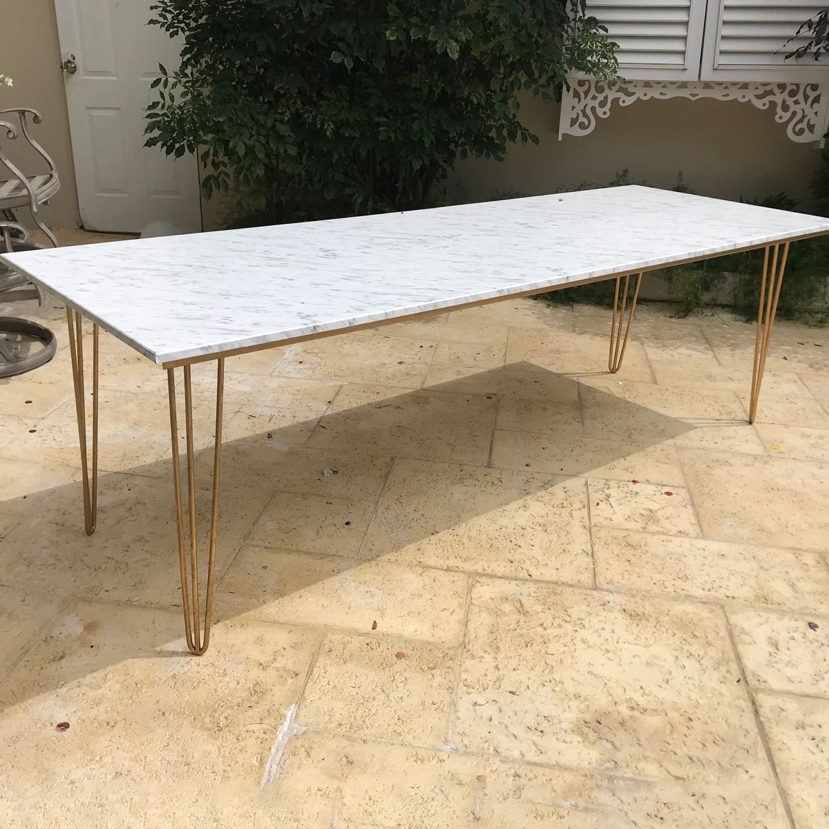 Marble Hairpin Table with a white marble-effect top and slim gold metal hairpin legs on a beige tiled patio