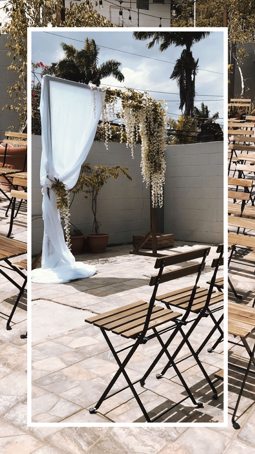 Outdoor ceremony with wooden chairs and a white draped floral arch