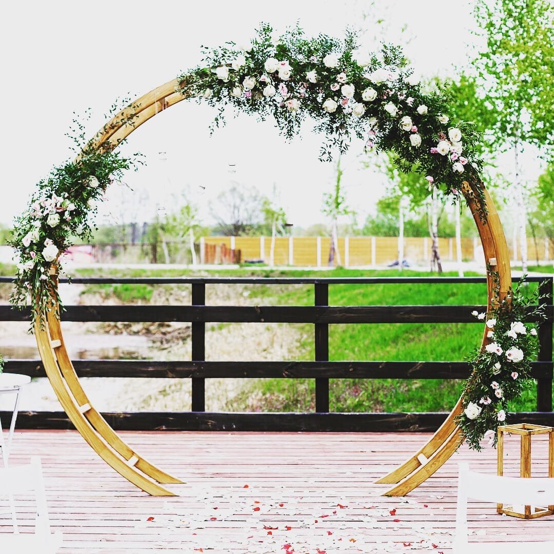 Oval Arch: A modern wooden circular arch used as a wedding ceremony arch, an entryway to the aisle or event, or a backdrop behind a pallet bar or sweetheart