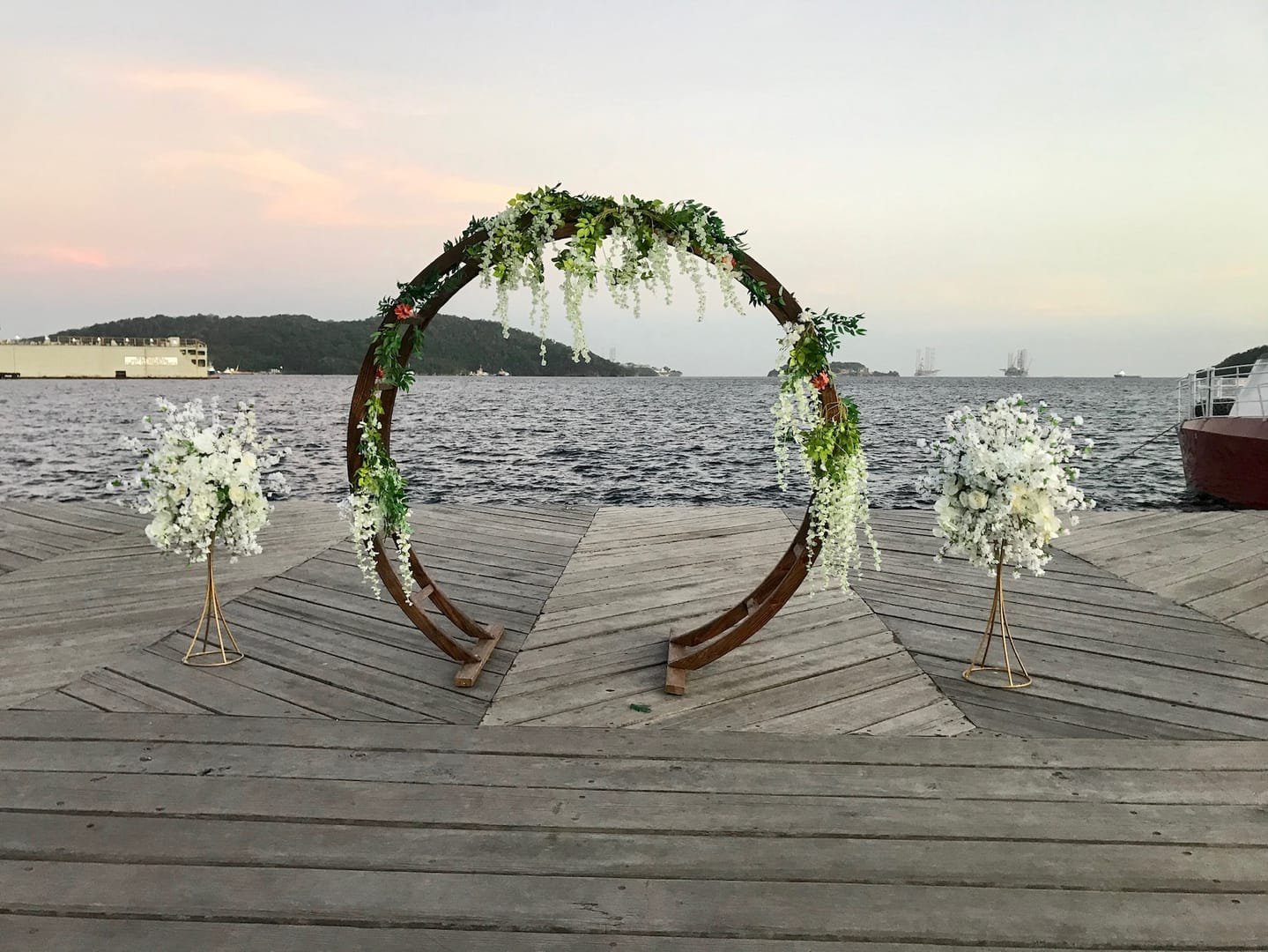 Oval Arch: A modern wooden circular arch used as a wedding ceremony arch, an entryway to the aisle or event, or a backdrop behind a pallet bar or sweetheart