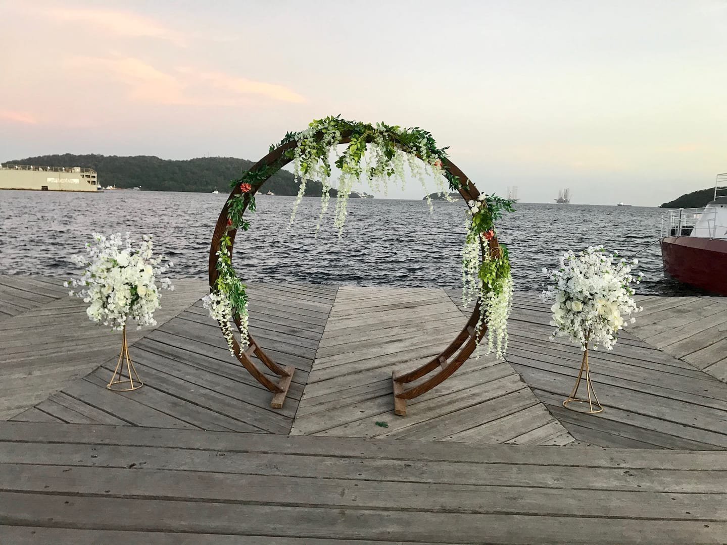 Oval Arch: A modern wooden circular arch used as a wedding ceremony arch, an entryway to the aisle or event, or a backdrop behind a pallet bar or sweetheart