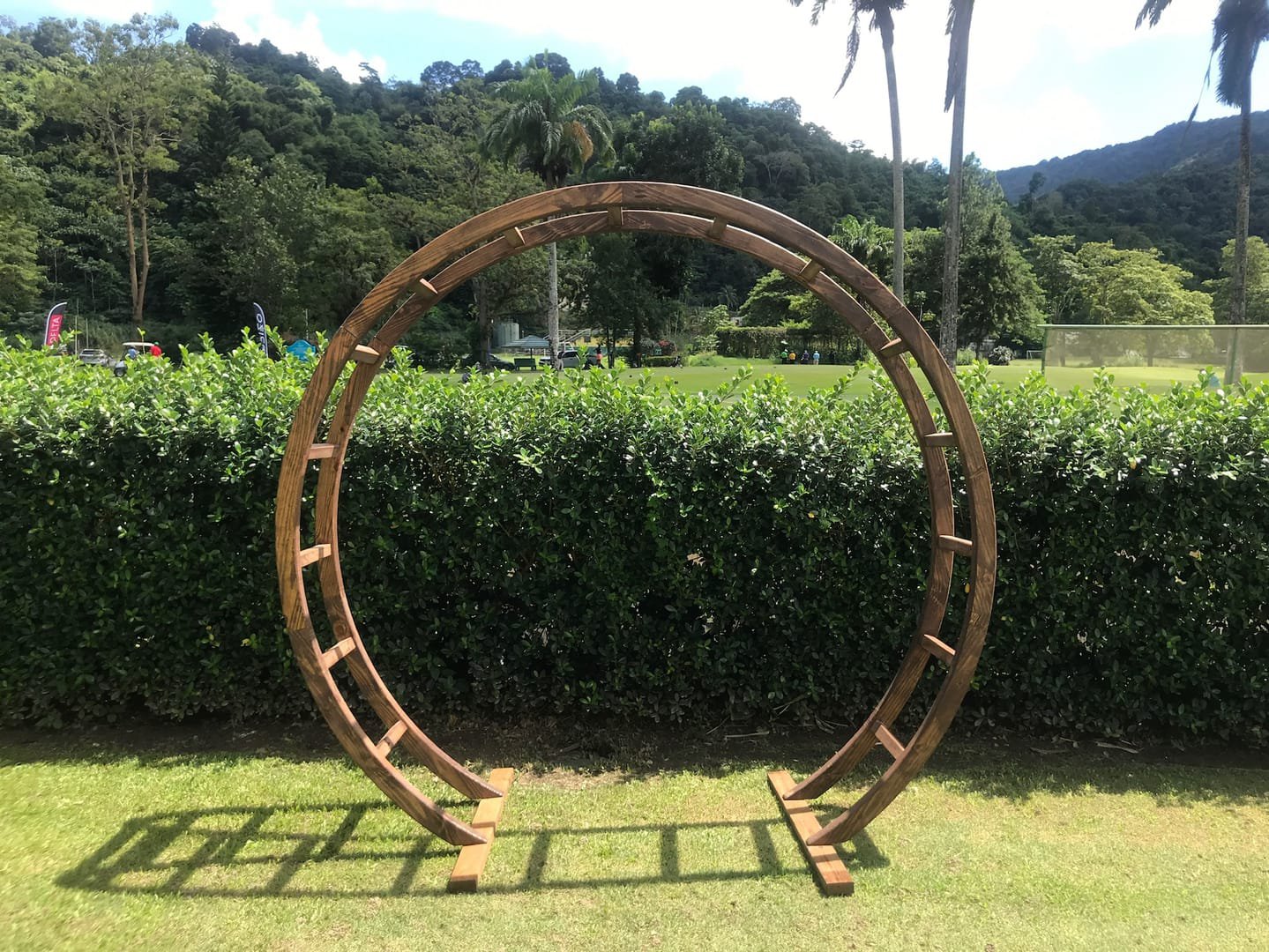 Oval Arch: A modern wooden circular arch used as a wedding ceremony arch, an entryway to the aisle or event, or a backdrop behind a pallet bar or sweetheart