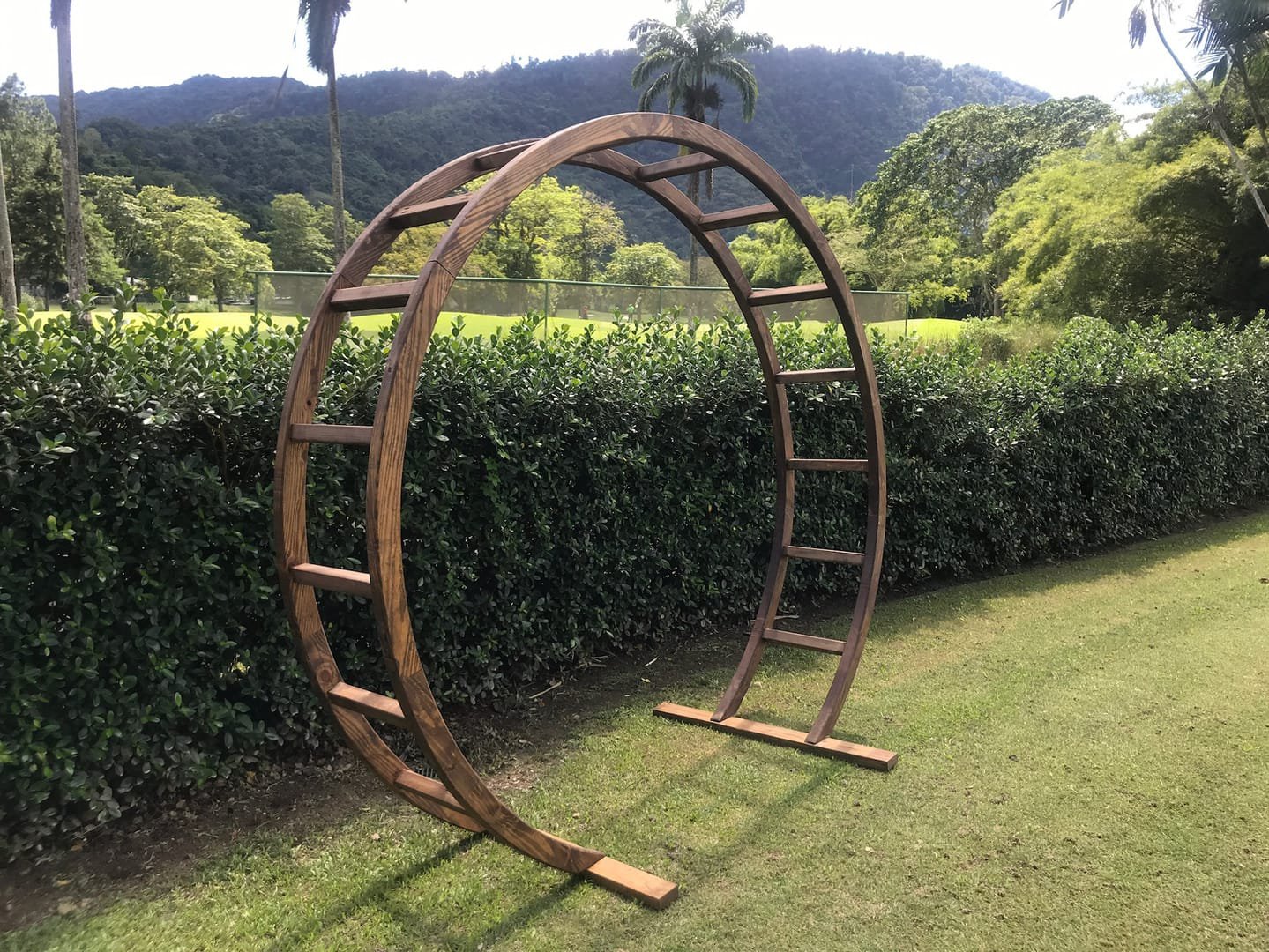 Oval Arch: A modern wooden circular arch used as a wedding ceremony arch, an entryway to the aisle or event, or a backdrop behind a pallet bar or sweetheart